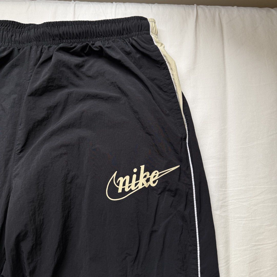 Nike Vintage Style Script Logo Nylon Track Pants Black Large (Category: Joggers) located in Pasig City. Submitted by notshynotmeee (Listing ID 1468957514, Image 2). Description: - Brand: Nike - Color: Black with cream and white side piping - Size: Large - Material: Durable nylon outer with breathable mesh lining - Design: Retro cursive Nike script logo on left thigh - Features: Elastic waistband with adjustable drawstring and zippered ankle cuffs