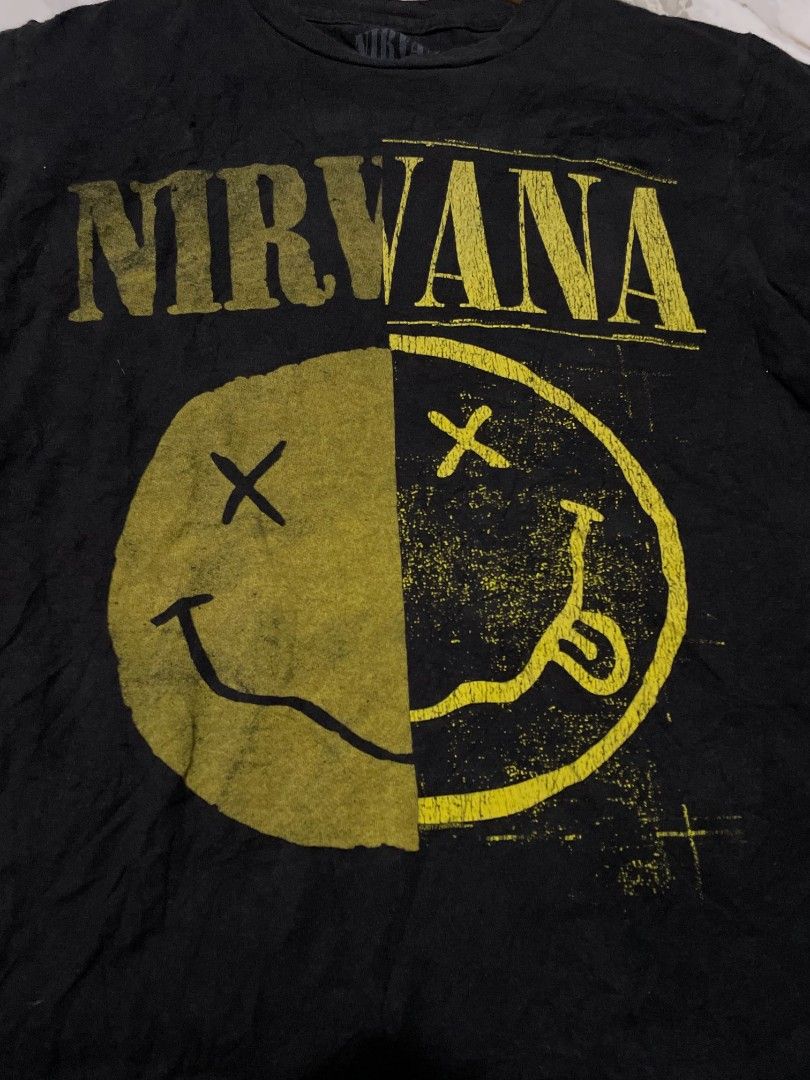Nirvana Graphic Tee Black Vintage Style (Category: Tshirts & Polo Shirts ) located in Manila. Submitted by mikeee03 (Listing ID 1468944208, Image 2). Description: - Color: Black with split yellow smiley face and Nirvana band logo - Material: 100% cotton (machine wash safe) - Condition: Pre-loved with noticeable wear, distressing, and small holes near the collar, upper chest, and sleeves - Style: Vintage grunge aesthetic, perfect for everyday casu