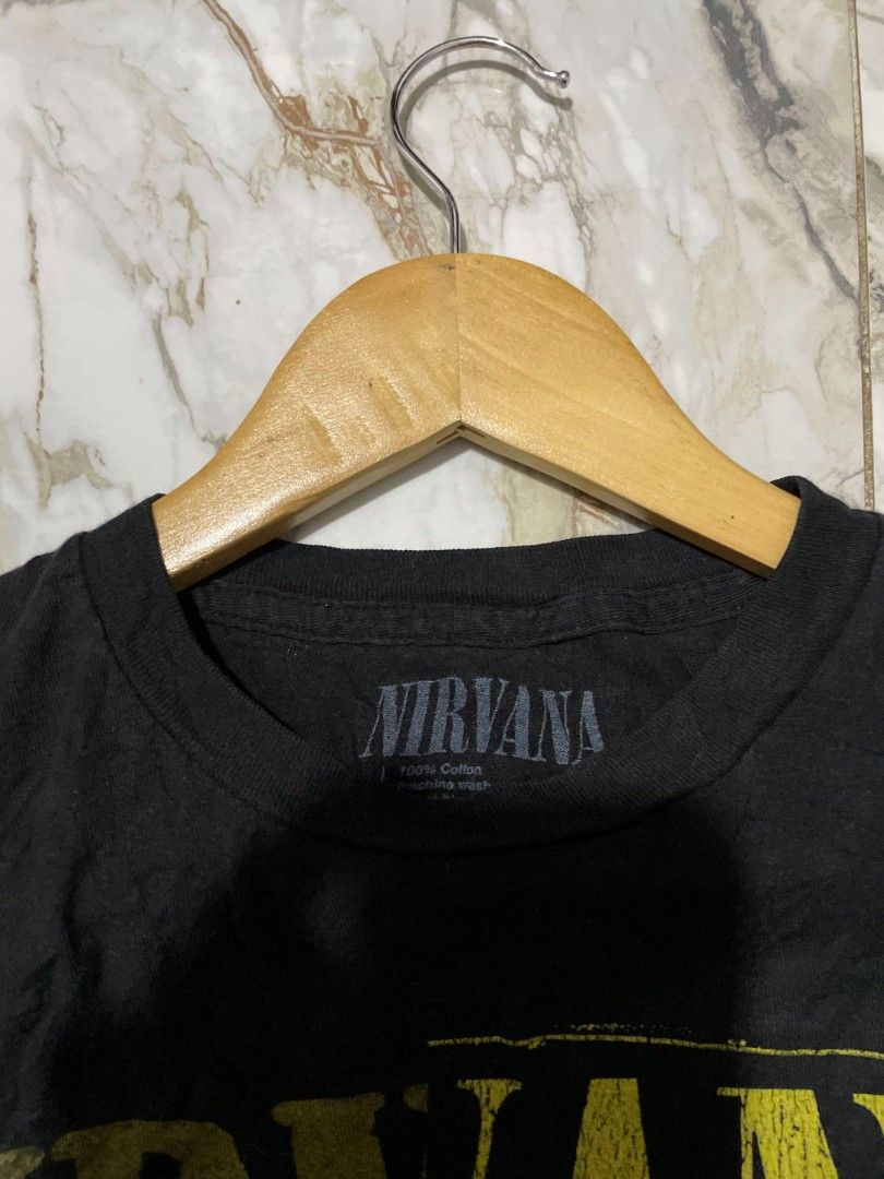 Nirvana Graphic Tee Black Vintage Style (Category: Tshirts & Polo Shirts ) located in Manila. Submitted by mikeee03 (Listing ID 1468944208, Image 3). Description: - Color: Black with split yellow smiley face and Nirvana band logo - Material: 100% cotton (machine wash safe) - Condition: Pre-loved with noticeable wear, distressing, and small holes near the collar, upper chest, and sleeves - Style: Vintage grunge aesthetic, perfect for everyday casu