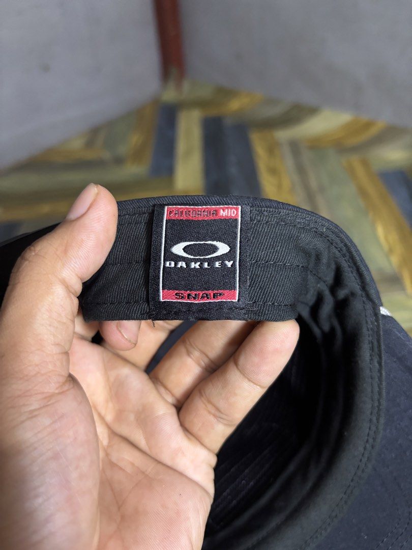 Oakley California Mid Snapback Cap Black (Category: Caps & Hats) located in Manila. Submitted by thriftkibs (Listing ID 1468944102, Image 3). Description: - Brand: Oakley - Style: Snapback cap with adjustable plastic closure - Color: Black with contrast white piping on brim and red Oakley tag - Details: Circular logo patch on front, inner mesh forehead band - Material: 100% cotton, made in China - Condition: Interior wash tag shows staining and w