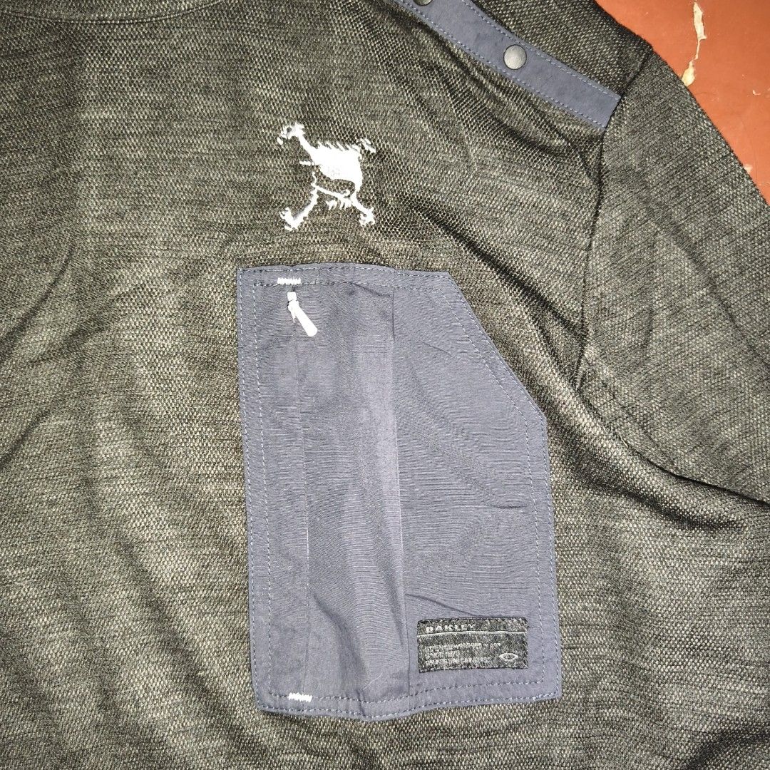 Oakley Charcoal Grey Funnel Neck Pullover Sweatshirt (Category: Coats, Jackets and Outerwear) located in Antipolo. Submitted by alphaomega_fox (Listing ID 1469024603, Image 3). Description: - Brand: Oakley -size: 20x28 - Style: Pullover with funnel neck and snap button closure - Color: Dark grey heather with contrast navy chest pocket - Pockets: 1 zippered chest pocket with small logo tag - Branding: White Oakley ellipse logo near bottom hem and 