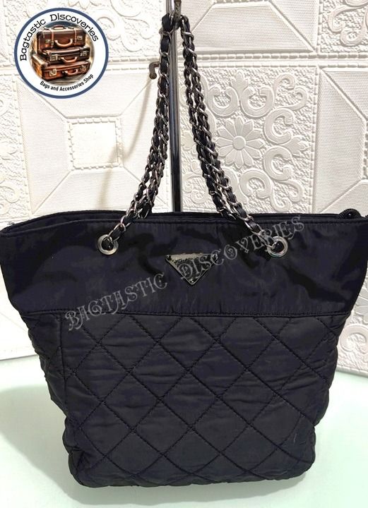 Preloved Quilted Nylon Chain Tote Bag Black (Category: Luxury Bags & Wallets) located in Santa Rosa. Submitted by bagtastic_discoveries (Listing ID 1469004863, Image 1). Description: - Color & Material: Black quilted nylon with a smooth upper section - Straps: Silver-tone chain interwoven with black leather - Details: Iconic triangle logo plaque on the front - Closure: Secure top zip closure - Interior: Roomy, clean fabric inside and out - Condit