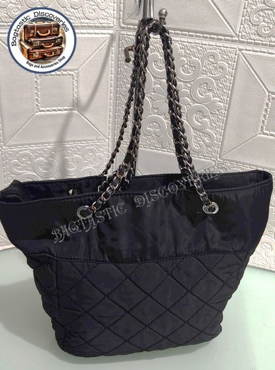 Preloved Quilted Nylon Chain Tote Bag Black (Category: Luxury Bags & Wallets) located in Santa Rosa. Submitted by bagtastic_discoveries (Listing ID 1469004863, Image 3). Description: - Color & Material: Black quilted nylon with a smooth upper section - Straps: Silver-tone chain interwoven with black leather - Details: Iconic triangle logo plaque on the front - Closure: Secure top zip closure - Interior: Roomy, clean fabric inside and out - Condit