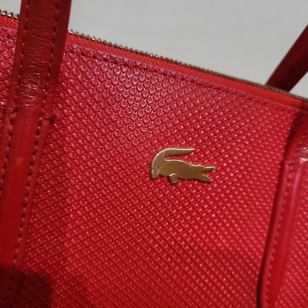Red Lacoste Textured Handbag with Strap (Category: Tote Bags) located in Manila. Submitted by windelynon66264 (Listing ID 1469029655, Image 2). Description: - Brand: Lacoste - Color: Bright red with textured finish and gold logo hardware - Straps: Double top handles and a detachable long strap - Closure & Interior: Secure zip closure, lined interior with one zipper pocket and slip pockets - Condition: Pre-loved with minor wear visible on the hand