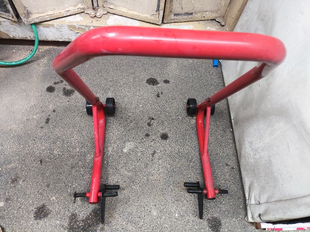 Red Motorcycle Rear Paddock Stand (Category: Bicycles) located in Pasig City. Submitted by giarpo (Listing ID 1469056235, Image 1). Description: - Item: Heavy-duty red steel rear motorcycle paddock stand - Stability: Dual wheels on each side for secure balancing - Features: Adjustable swingarm spools/supports with securing pins - Condition: Fully functional and solid, with minor surface rust and wheel wear from garage use - Ideal for: Easy home m