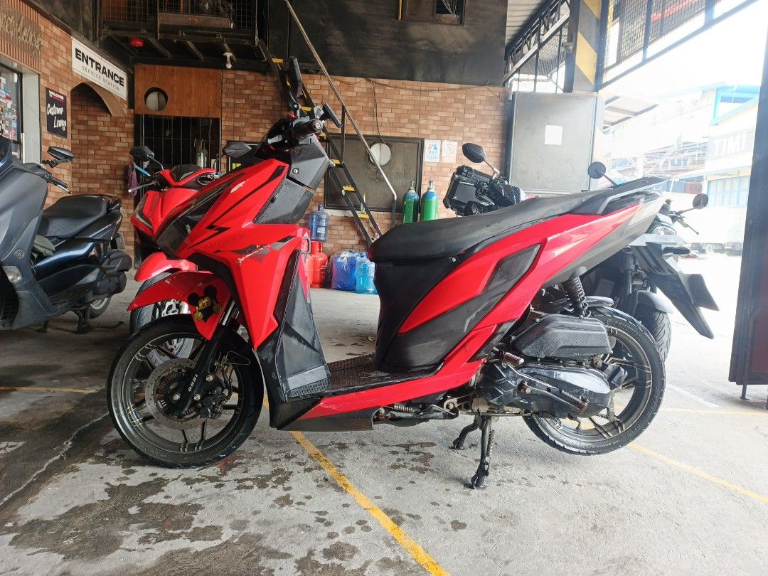 Red Motorcycle Scooter (Category: Motorbikes for Sale) located in Manila. Submitted by pieces1996 (Listing ID 1468975558, Image 2). Description: Bright red automatic scooter. Black seat and floorboard. Stock wheels with dual-tone rims. VMax decal on the front fairing. Standard handlebars with black mirrors. Center stand attached. Clean paint job overall, ready for daily commutes around town..