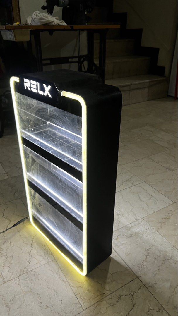 RELX Lighted Display Stand Cabinet (Category: Shelves, Cabinets & Racks) located in Pasig City. Submitted by galgadowt (Listing ID 1469012591, Image 2). Description: Came from the company itself. Bought for P6k Selling for P2,990 last price Good display for business. Or for collectors Brand: RELX - Type: Illuminated display shelf for vapes and accessories - Design: Black frame with LED lighting on outer edges and tiers - Features: Clear acrylic f