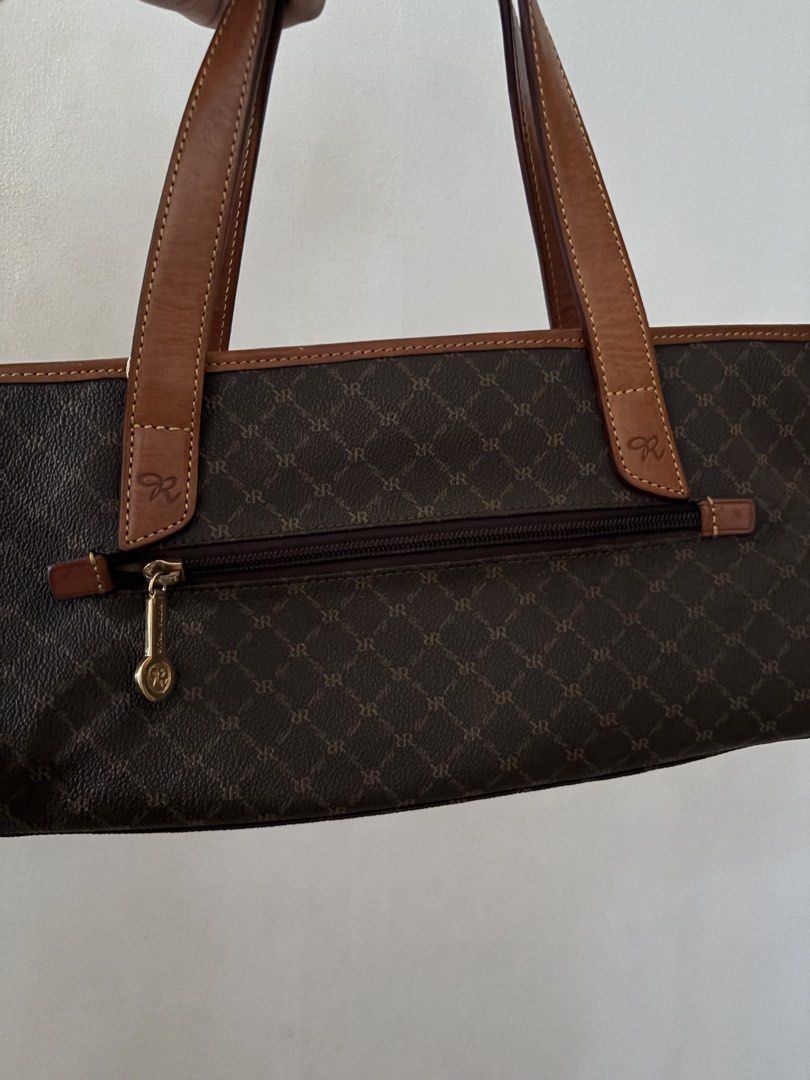 Rioni Monogram Tote Bag Brown (Category: Tote Bags) located in Quezon City. Submitted by clareb (Listing ID 1468966618, Image 2). Description: - Brand: Rioni Monogram Tote Bag - Color: Classic brown monogram with tan leather trim and double shoulder straps - Hardware: Elegant gold-tone details with front Rioni logo emblem - Closure: Secure zip-top closure - Interior: Clean Rioni logo fabric lining with multiple slip pockets and a zippered pocket 