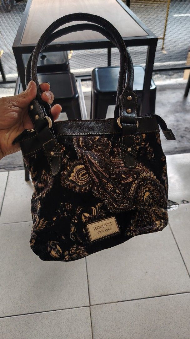Rosetti Est 1994 Black Paisley Handbag (Category: Shoulder Bags) located in Manila. Submitted by purediamond888 (Listing ID 1469037566, Image 1). Description: - Brand: Rosetti Est 1994 - Material: Black fabric with paisley and floral print - Trim: Dark brown faux leather straps and accents - Hardware: Gold-tone brand plaque - Closure: Zip top for secure everyday use - Interior: Spacious compartment for daily essentials - Condition: Minor wear on 