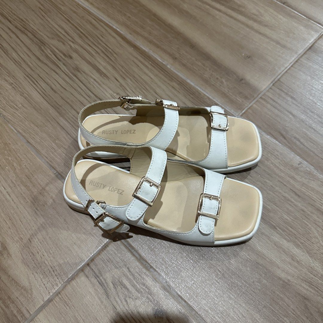 Rusty Lopez White Strappy Sandals Size 6 (Category: Flats & Sandals) located in Pasig City. Submitted by nina.declutter (Listing ID 1469033614, Image 2). Description: - Brand: Rusty Lopez - Color: White with light beige footbed - Size: 6 - Design: Square toe, multiple straps with gold-tone buckle details - Closure: Adjustable slingback buckle - Condition: Uppers are in solid condition, with moderate wear on the bottom soles.