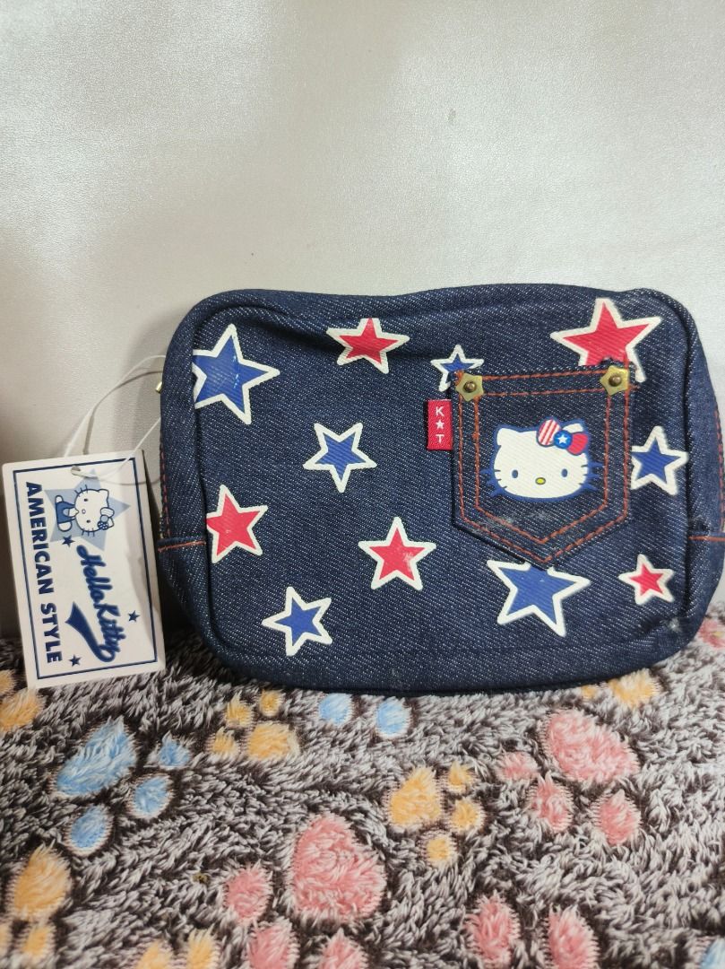 Sanrio Hello Kitty American Style Denim Pouch (Category: Purses & Pouches) located in San Leonardo. Submitted by burgossanleonardo.12345 (Listing ID 1469064491, Image 2). Description: - Condition: Brand new with tag (BNWT) - Design: Dark blue denim with red/blue stars and Kitty American Style tag - Features: Front pocket with Kitty face, secure top zip closure, and large script lettering on the back - Interior: Cute striped lining with original S