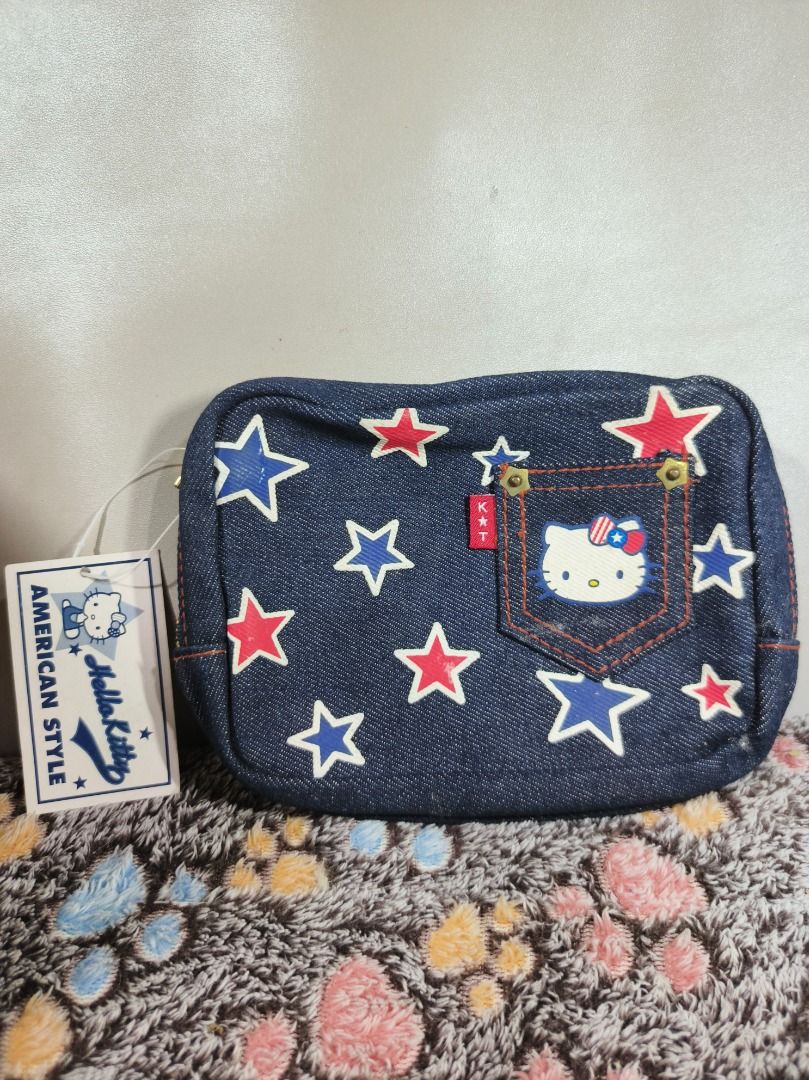 Sanrio Hello Kitty American Style Denim Pouch (Category: Purses & Pouches) located in San Leonardo. Submitted by burgossanleonardo.12345 (Listing ID 1469064491, Image 1). Description: - Condition: Brand new with tag (BNWT) - Design: Dark blue denim with red/blue stars and Kitty American Style tag - Features: Front pocket with Kitty face, secure top zip closure, and large script lettering on the back - Interior: Cute striped lining with original S