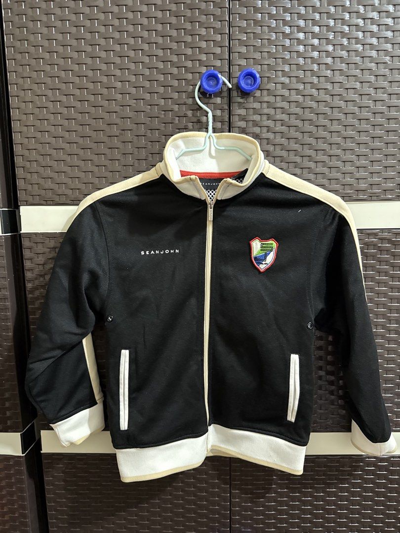 Sean John black track jacket with patches (Category: Coats, Jackets and Outerwear) located in Manila. Submitted by vastwind-676c (Listing ID 1468955061, Image 1). Description: - Brand: Sean John - Style: Classic sportswear track jacket - Color: Black with cream and white accents - Features: Full zip closure, high collar, two front pockets, and white mesh interior lining - Branding: Embroidered Sean John lettering and colorful crest patch on the c