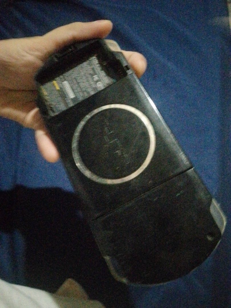 Sony PSP Handheld Console (Category: PlayStation) located in Quezon City. Submitted by mahiwagangkamote (Listing ID 1469023396, Image 2). Description: - Item: Black Sony portable gaming console - Condition: Heavy wear, dirt accumulation, and rust near the charging port - Screen: Numerous scratches and dust present - Battery: Cover is missing, battery is exposed - Purpose: Selling strictly as-is for spare parts or a restoration project - Note: Req