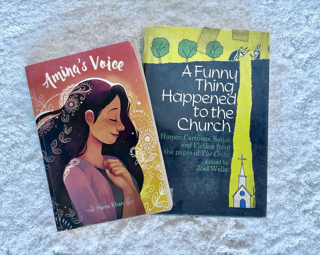 Stories About Religious Communities Book Bundle of 2 (Category: Storybooks) located in Naga. Submitted by klutzdeclutters (Listing ID 1468949892, Image 1). Description: Includes: - Amina’s Voice by Hena Khan - A Funny Thing Happened to the Church edited by Joel Wells Condition: - Covers show heavy wear and distinct tape repairs, with clear adhesive tape visible across the top edge of the yellow book, along with noticeable scuffing and corner blun