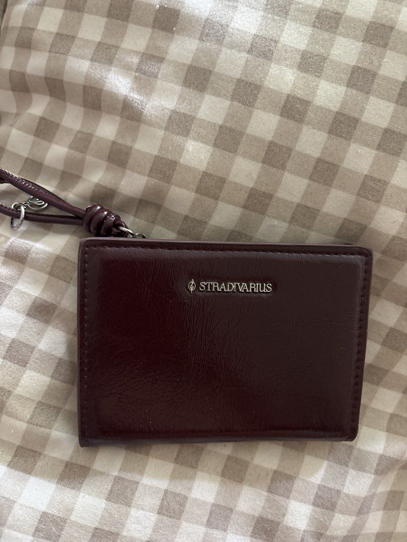 Stradivarius Burgundy Wallet (Category: Wallets & Card holders) located in Manila. Submitted by kt.dd (Listing ID 1468948643, Image 1). Description: - Brand: Stradivarius - Color: Rich burgundy faux leather - Design: Compact fold-over style with clean stitched edges - Details: Silver-tone front branding and a matching removable wrist strap - Functionality: Keeps cards and cash organized, fits easily in small bags.
