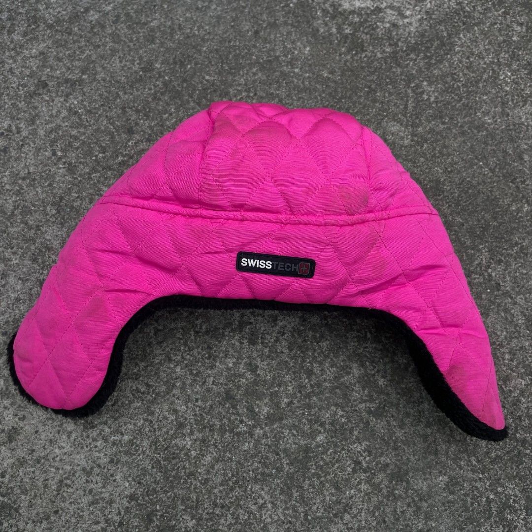 Swiss Tech Trapper Hat (Category: Hats & Beanies) located in Tanza. Submitted by ThriftPieces (Listing ID 1468974991, Image 2). Description: - Brand: Swiss Tech - Color: Bright pink with black faux fur - Material: Quilted nylon exterior with soft faux fur lining - Features: Warm ear flaps and classic front logo patch - Style: Standout look perfect for cold weather, snow, or city wear.