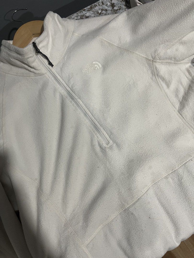 The North Face White Quarter-Zip Fleece Pullover (Category: Coats, Jackets and Outerwear) located in Maasin. Submitted by niconii090 (Listing ID 1468985333, Image 3). Description: - Brand: The North Face - Color: White - Style: Half-zip fleece pullover with mock neck and kangaroo pocket - Extra Features: Thumbholes on sleeves with zippered cuffs, embroidered chest logo - Condition: Pre-loved with a couple of small stains on the fabric and sleeve 