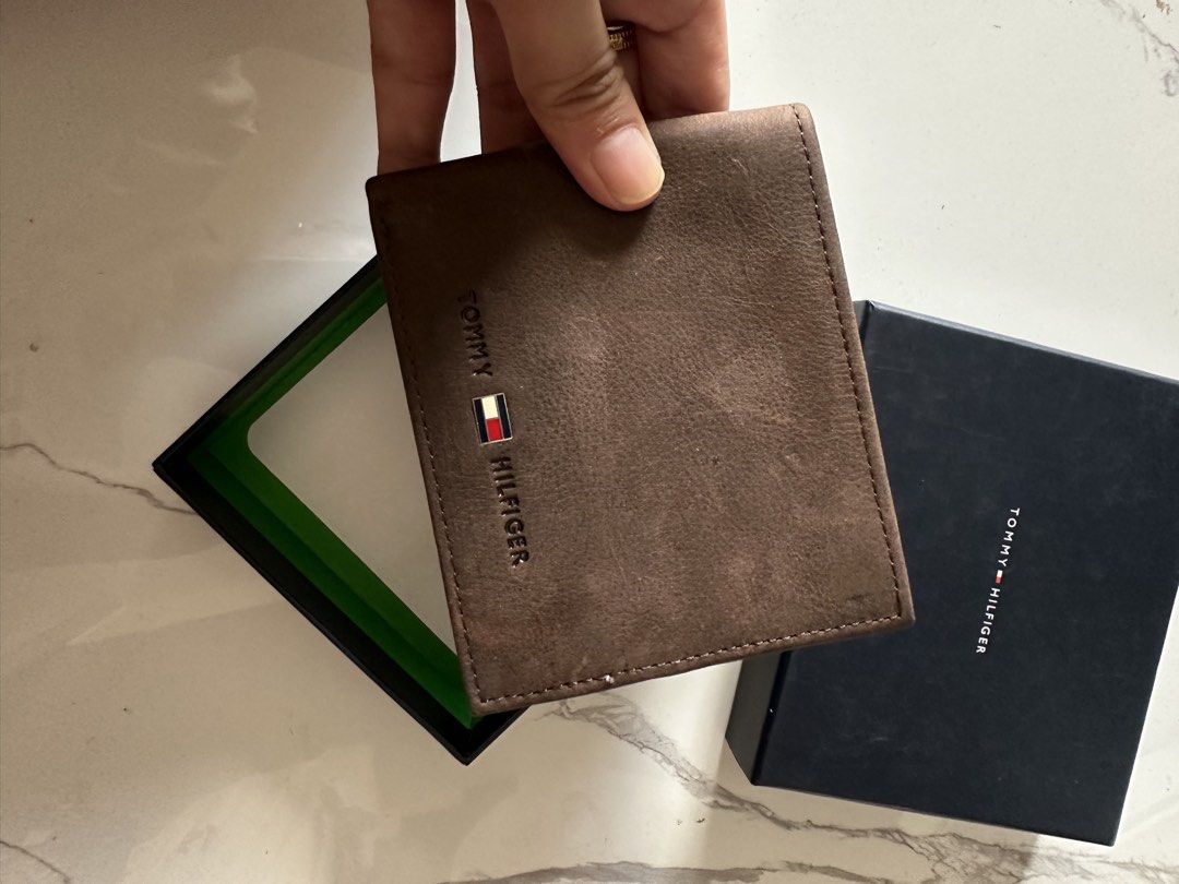 Tommy Hilfiger Brown Leather Bifold Wallet with Box (Category: Wallets & Card Holders) located in Vinzons. Submitted by melodylarg85741 (Listing ID 1468977911, Image 3). Description: - Brand: Tommy Hilfiger - Material: Genuine brown leather - Design: Bifold with embossed front logo and brand hardware detail - Interior: Multiple card slots and trendy striped fabric lining - Special Detail: Est. 1985 stamp inside - Packaging: Includes original blac