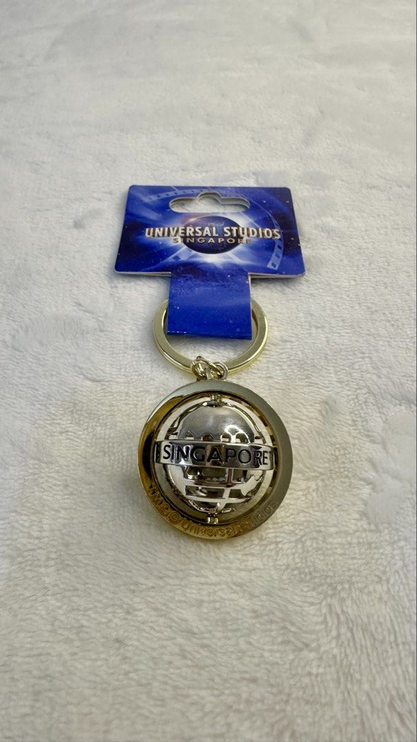 Universal Studios Singapore Globe Keychain (Category: Character Goods) located in Makati City. Submitted by cecille1998 (Listing ID 1469005575, Image 3). Description: - Official Universal Studios Singapore merchandise - Features a fun spinning metal globe design with engraved lettering - Elegant gold tone ring and hardware - Brand new and unused - Comes with original backing card, barcode, and price label intact - Ideal as a gift or a cute additi