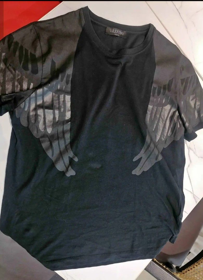 Valentino 2015 Eagle Wing T-Shirt (Category: Tshirts & Polo Shirts ) located in Manila. Submitted by gfinds. (Listing ID 1469071718, Image 2). Description: - Brand: Valentino - Color: Black - Material: 100% Cotton (Made in Italy) - Design: Engineered falcon and wing graphic print across front, shoulders, and back - Style: Short sleeves, crew neck - Era: Iconic mid-2010s luxury designer piece - Condition: Includes original wash care label and bran