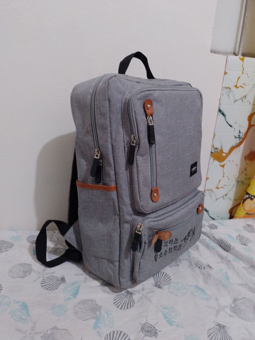 Veloche Grey Canvas Laptop Backpack (Category: Backpacks) located in Imus. Submitted by bestfinds_yeth0724 (Listing ID 1469153579, Image 2). Description: Grey canvas backpack from Veloche. Has brown faux leather accents, multiple zippered exterior pockets, and a top grab handle. Inside has a padded laptop sleeve with a velcro strap. Back straps are adjustable and padded. Korean text printed on the lower front pocket. MOP gcash Issue; please refer