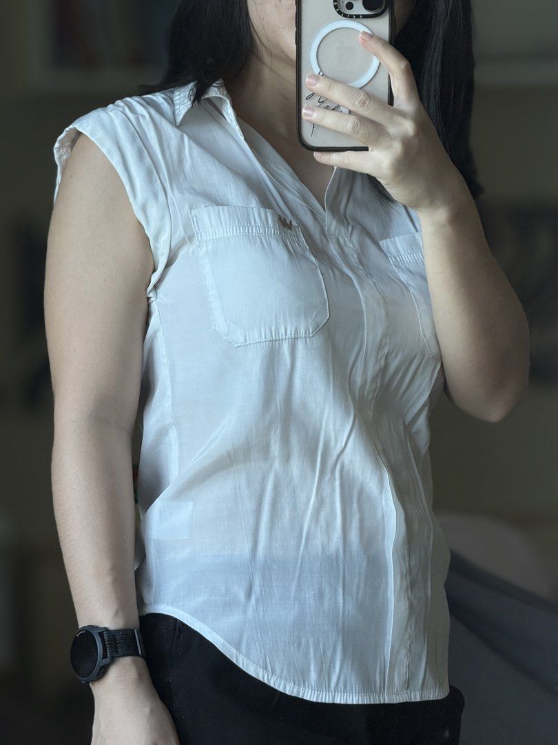 White sleeveless button-down shirt with front pockets (Category: Sleeveless) located in Pasig City. Submitted by laagn.ph (Listing ID 1469089416, Image 2). Description: - Color: White - Style: Sleeveless button-down top with a classic collar and rounded hem - Details: Two chest pockets with button flaps and small logo embroidery above the right pocket - Fabric: Light and airy for all-day comfort - Versatility: Easy to pair with shorts, jeans, or 