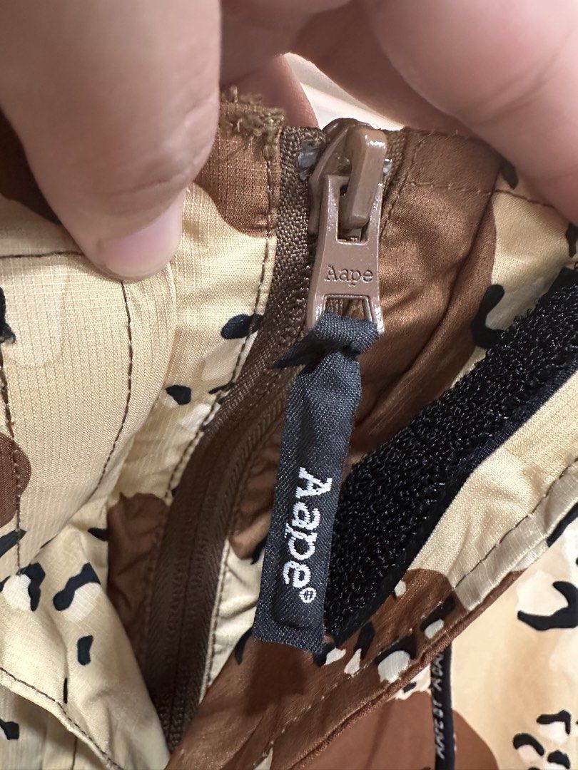 AAPE By A Bathing Ape Desert Camo Jacket (Category: Coats, Jackets and Outerwear) located in Bulacan. Submitted by adoseofluxxee (Listing ID 1465498884, Image 3). Description: - Brand: AAPE By A Bathing Ape - Item: Desert Camo Jacket - Size: L - Color: Brown and beige camouflage - Details: Full zip closure, branded pull, drawstring hood - Branding: Bold white AAPE lettering on front placket - Pockets: Multi-pocket design including a utility sleev