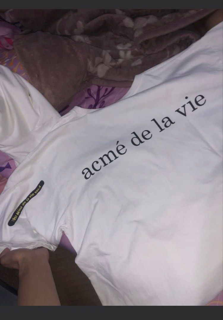 ADLV White Donut Graphic Tee (Category: Tshirts & Polo Shirts ) located in Davao. Submitted by kennysmith3928 (Listing ID 1465475474, Image 2). Description: - Brand: Acme de la Vie (ADLV) - Color: White - Size: 2 (on tag) - Material: 100% cotton - Design: Cute front graphic of a kid holding pink frosted and chocolate donuts, large branding printed across the back, and small text detail on the right sleeve - Condition: Interior brand label and car