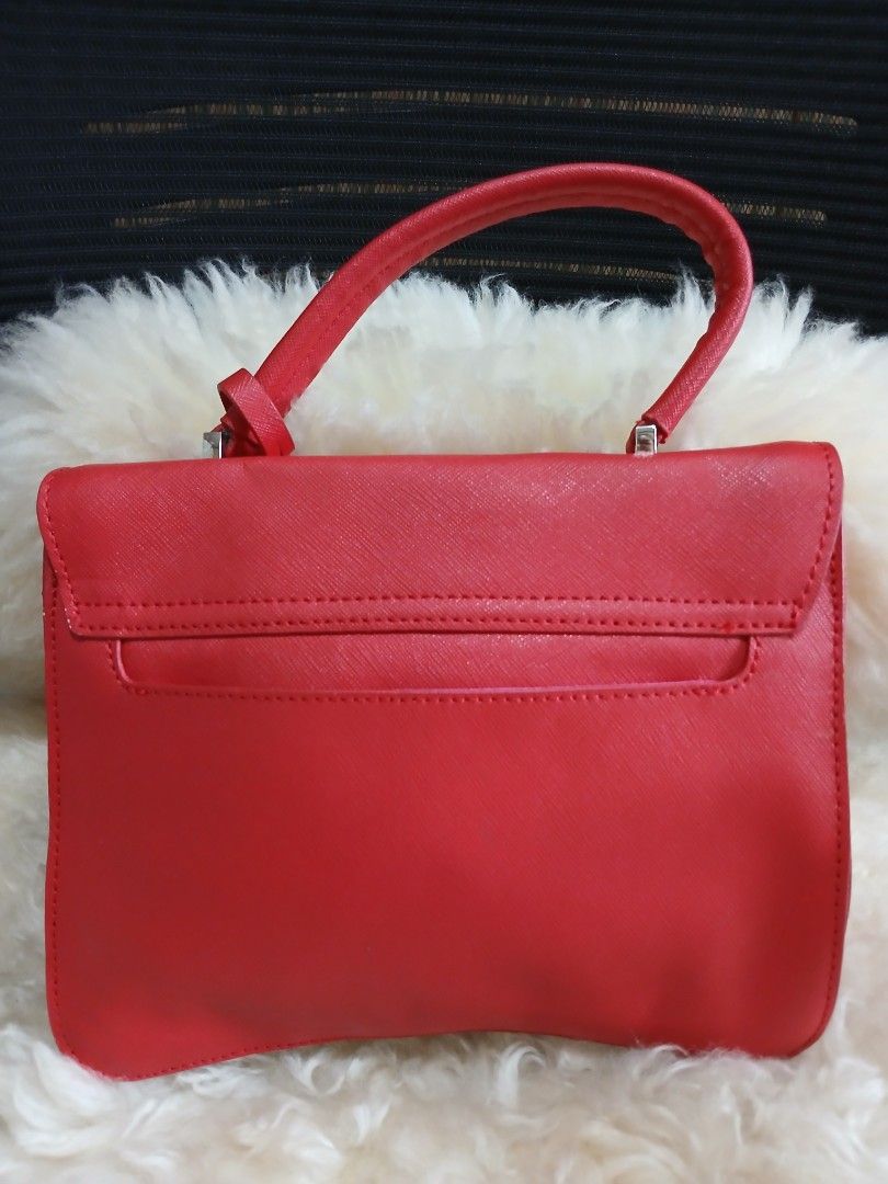 Agnes b. Voyage Red Handbag (Category: Luxury Bags & Wallets) located in Taguig. Submitted by demsclosetph (Listing ID 1465425980, Image 2). Description: Bright red satchel bag from agnes b. voyage. Saffiano leather texture on the outside. Vibrant pink fabric lining inside with branding print. Metal twist lock closure on the front flap, shaped like the signature logo. Includes top handle and back slip pocket. Inside zip compartment for small item