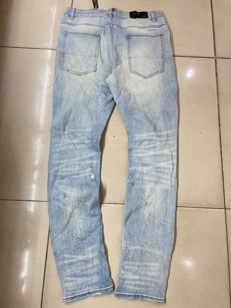 AMIRI Distressed Light Wash Denim Jeans (Category: Jeans) located in Cainta. Submitted by riszizlux (Listing ID 1465472866, Image 2). Description: - Brand: AMIRI - Wash: Light wash denim with authentic distressing and knee rips - Details: Unique white paint splatter effect on front and back legs - Features: Classic 5-pocket styling and leather logo patch on the back waistband - Condition: Brand new with tags still attached.