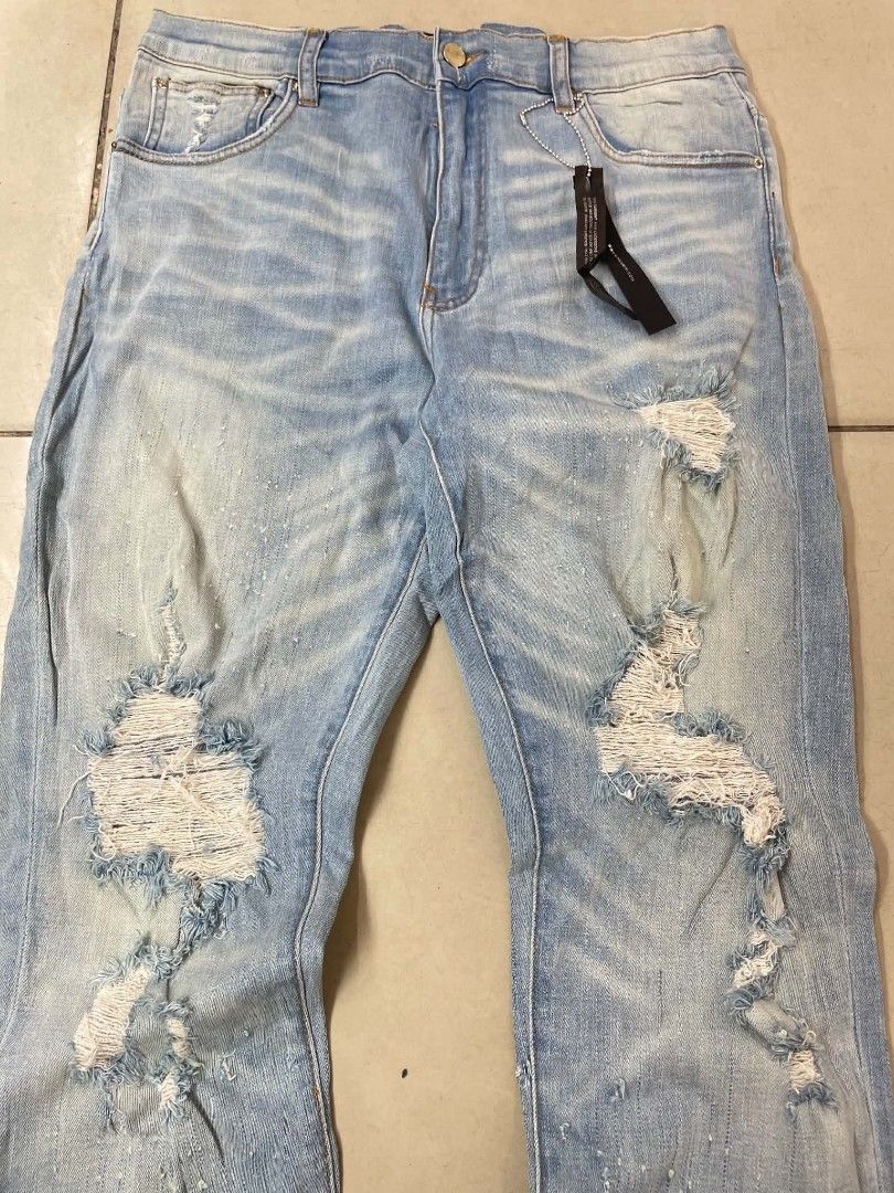 AMIRI Distressed Light Wash Denim Jeans (Category: Jeans) located in Cainta. Submitted by riszizlux (Listing ID 1465472866, Image 3). Description: - Brand: AMIRI - Wash: Light wash denim with authentic distressing and knee rips - Details: Unique white paint splatter effect on front and back legs - Features: Classic 5-pocket styling and leather logo patch on the back waistband - Condition: Brand new with tags still attached.