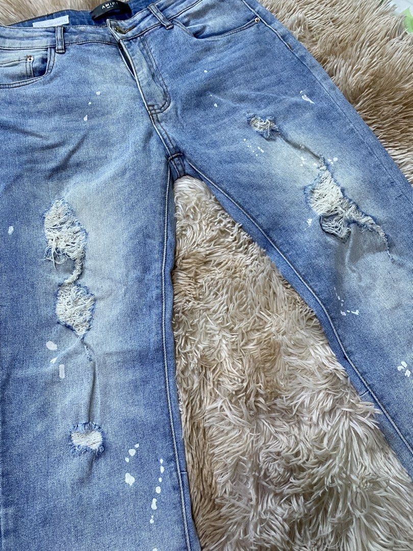 AMIRI Distressed Paint Splatter Jeans Size 32 (Category: Jeans) located in Santa Ana. Submitted by tunes_vtg (Listing ID 1465462539, Image 3). Description: - Brand: AMIRI - Color/Wash: Light blue wash - Size: 32 - Details: Paint splatter effect, distressed ripped knees, and frayed areas - Construction: Classic five-pocket style with button fly - Branding: Leather waist label and custom branded hardware - Condition: Clean hems, well-maintained - N