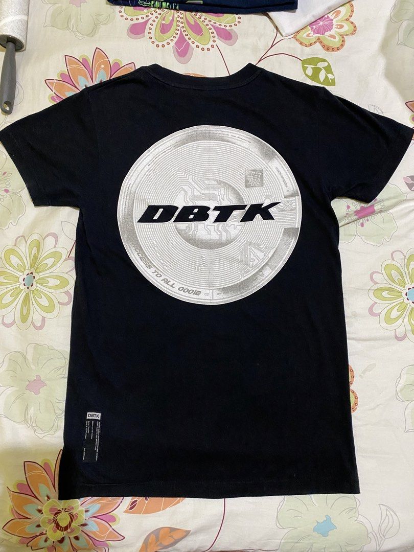 Authentic DBTK Cipher Black Shirt (Category: Tshirts & Polo Shirts ) located in Malolos. Submitted by ainttg (Listing ID 1465570905, Image 3). Description: - Brand: DBTK - Color: Black - Size: XS (inner collar tag) - Design: Bold white front logo and large circular circuit graphic on the back - Details: Small branding tag near the hemline - Condition: Pre-loved with mild fabric fuzziness - Style: Comfortable basic piece for casual everyday wear.