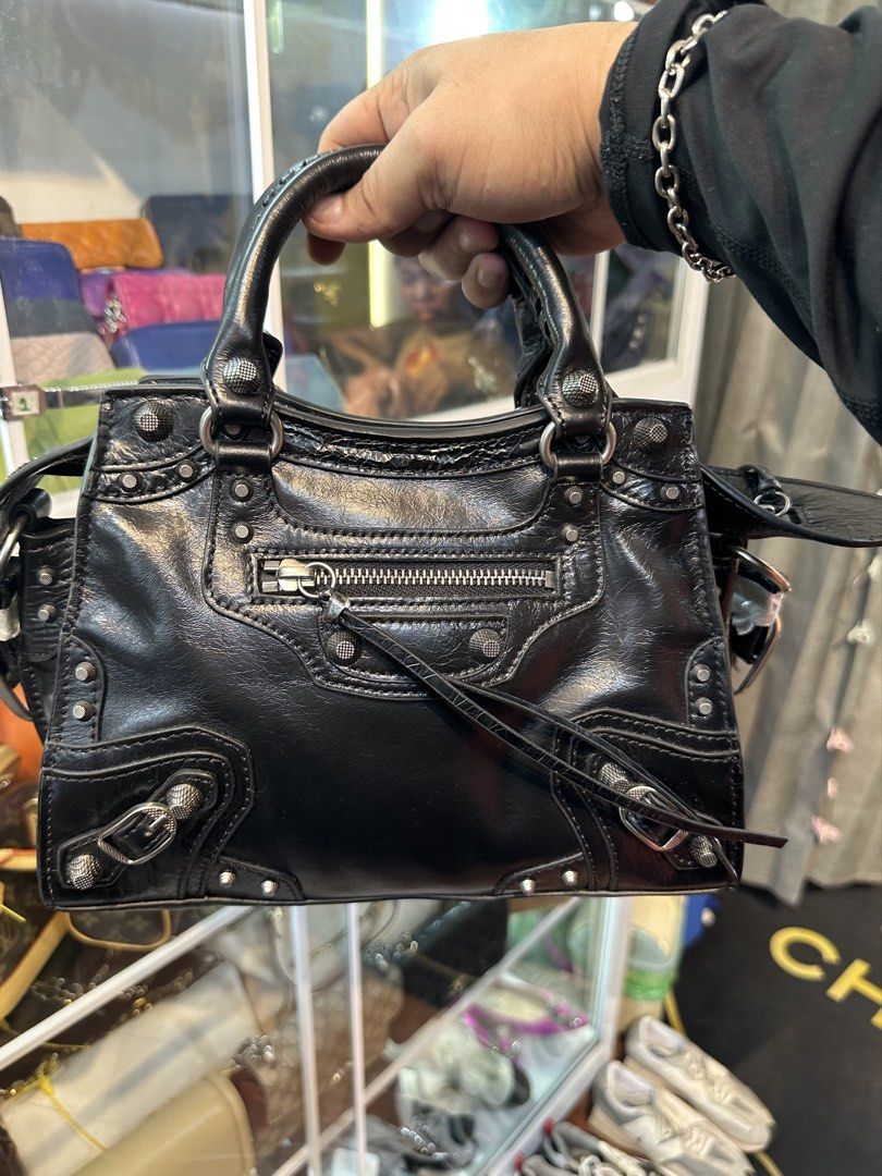 Balenciaga Black City Handbag (Category: Luxury Bags & Wallets) located in Daet. Submitted by thrifthings2018 (Listing ID 1465482056, Image 1). Description: - Edgy silver hardware, studs, and signature double BB logo zip pullers - Versatile carry options with dual rolled top handles and a matching shoulder strap - Secure top zip closure with exterior front zip pocket - Black fabric-lined interior featuring an inner zippered pocket - Iconic motorc