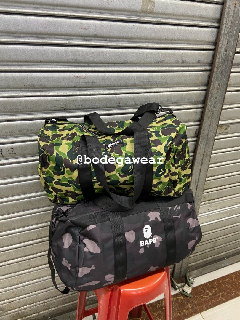 BAPE Camo Duffle Bag Green and Black (Category: Sling Bags) located in Manila. Submitted by bodegawear_mnl (Listing ID 1465407578, Image 3). Description: - Available Colors: Green Camo and Black Camo - Material: Durable, high-quality canvas with sturdy black carrying handles - Features: Bold BAPE logo patches on the front and a detachable shoulder strap (included with the black bag) - Versatility: Perfect size for the gym, travel, or everyday use