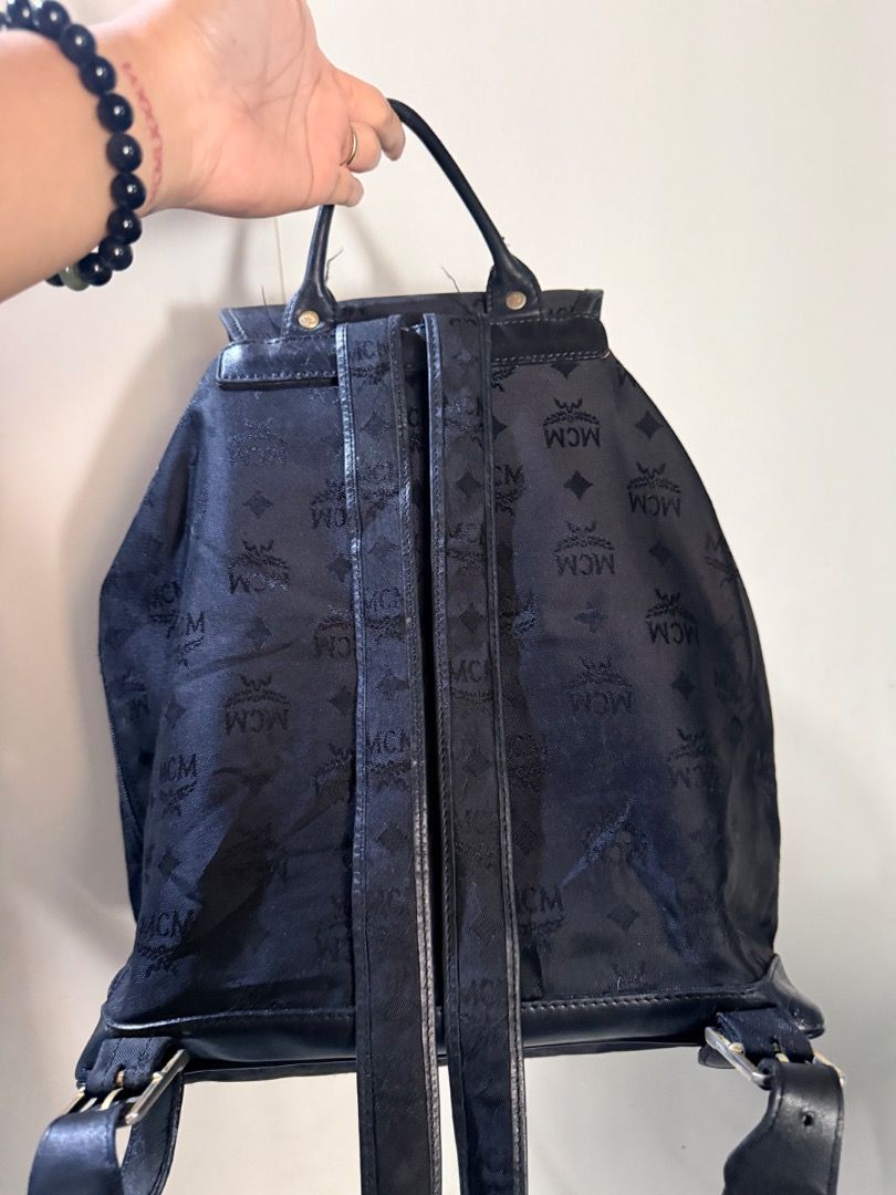 Black MCM Monogram Nylon Backpack with Front Pockets (Category: Backpacks) located in Manila. Submitted by _outofthecloset. (Listing ID 1465421748, Image 2). Description: - black MCM monogram backpack - Secure drawstring closure with buckled flap and magnetic snap - Two exterior front utility pockets with MCM logo plate - Elegant gold-tone hardware throughout - Fabric-lined interior with a convenient zippered pocket - Features a sturdy top handle