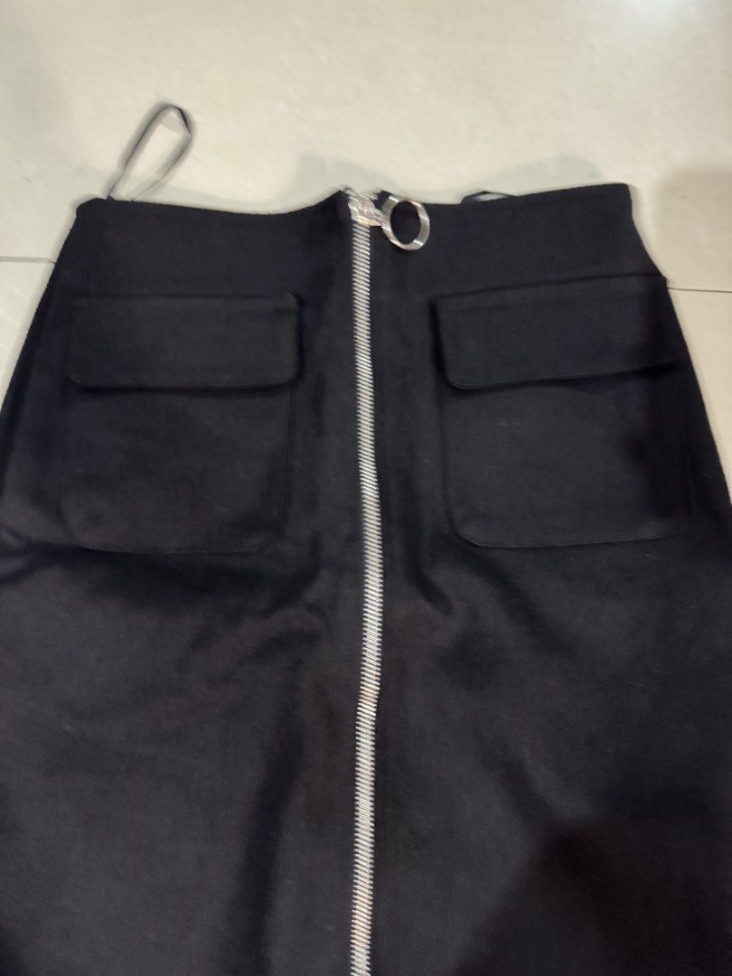 Black Zipper Front Skirt (Category: Skirts) located in Quezon City. Submitted by sweetlyluxe (Listing ID 1465492796, Image 2). Description: - Brand: HANHAO - Size: M - Color: Plain Black - Features: Front zipper with large ring pull, two front patch pockets with flaps, back darts for a flattering shape - Condition: Clean inside lining, brand label intact - Style: Versatile and chic, easy to pair with any top.