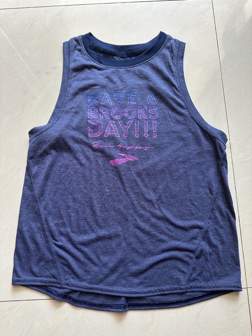 Brooks Running Top Size S (Category: Activewear) located in Rosales. Submitted by dariang22 (Listing ID 1465395131, Image 2). Description: - Brand: Brooks - Color: Heather blue - Size: S - Design: 'HAVE A BROOKS DAY!!!' graphic with Run Happy slogan and logo - Material: Lightweight, breathable athletic fabric - Fit: Relaxed fit with a comfortable racerback style - Condition: Excellent/Great for workouts and running.