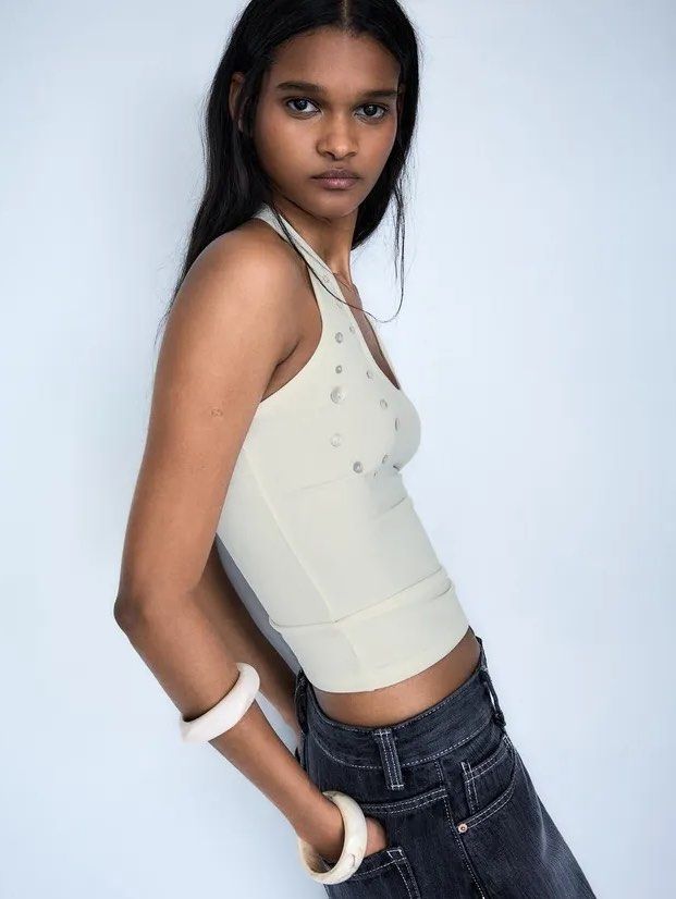 Bershka Button Halter Tank Top (Category: Sleeveless) located in Santiago. Submitted by moguaddict (Listing ID 1465437384, Image 2). Description: - Style: Halter neck tank top with a scoop neckline - Details: Covered all over the front with assorted small buttons in various sizes - Fit: Form-fitting, sleeveless cut - Material: Comfortable ribbed fabric - Versatility: Perfect for both casual wear and dressing up.