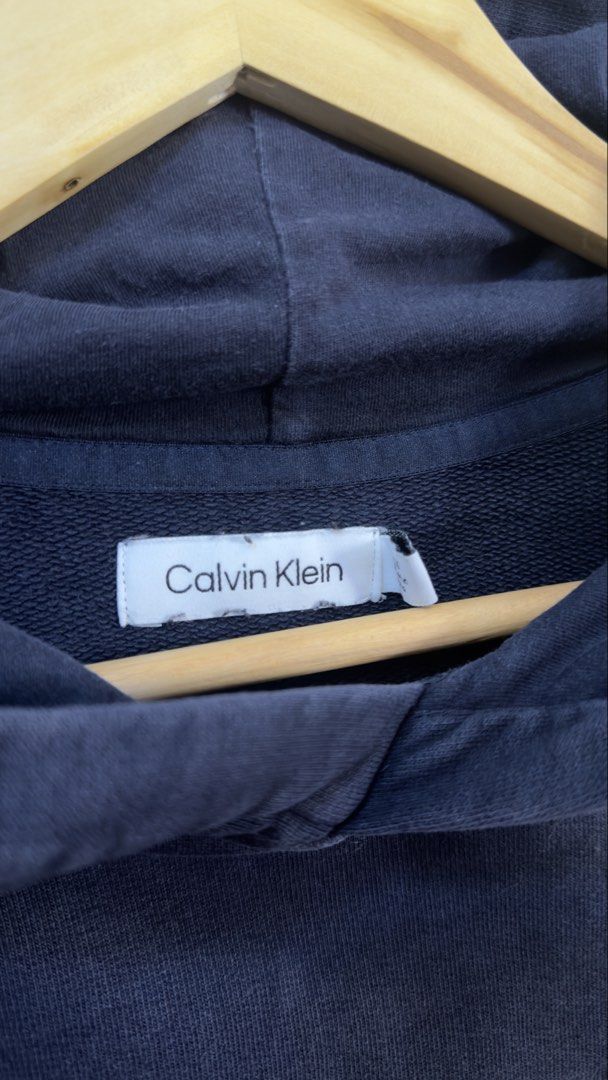 Calvin Klein Navy Blue Logo Hoodie (Category: Coats, Jackets and Outerwear) located in Paranaque City. Submitted by preluxeshop_ph (Listing ID 1465555367, Image 3). Description: Calvin Klein Navy Blue Logo Hoodie - Color: Dark blue with white logo across chest - Material: 100% cotton (Made in India) - Features: Drawstring hood, front kangaroo pocket, ribbed cuffs and hem - Fit: Regular fit, classic streetwear style - Condition: Excellent everyday