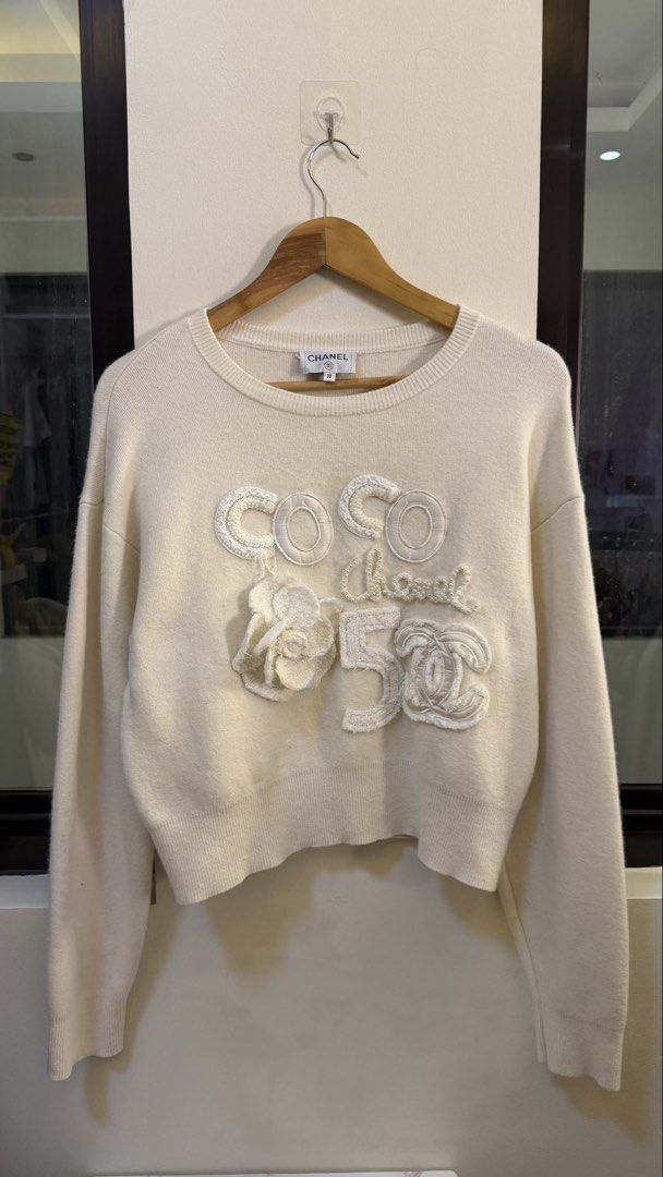 Chanel White COCO 5 sweater size 38 (Category: Longsleeves) located in Paranaque City. Submitted by preluxeshop_ph (Listing ID 1465559508, Image 2). Description: Chanel White COCO 5 sweater size 38 Made in Italy. Long sleeves with ribbed cuffs and hem. Front features textured appliqués spelling out COCO, chanel, number 5, along with a camellia flower detail. Back has a couple of faint stains near the shoulder and bottom hem. Classic crew neck des