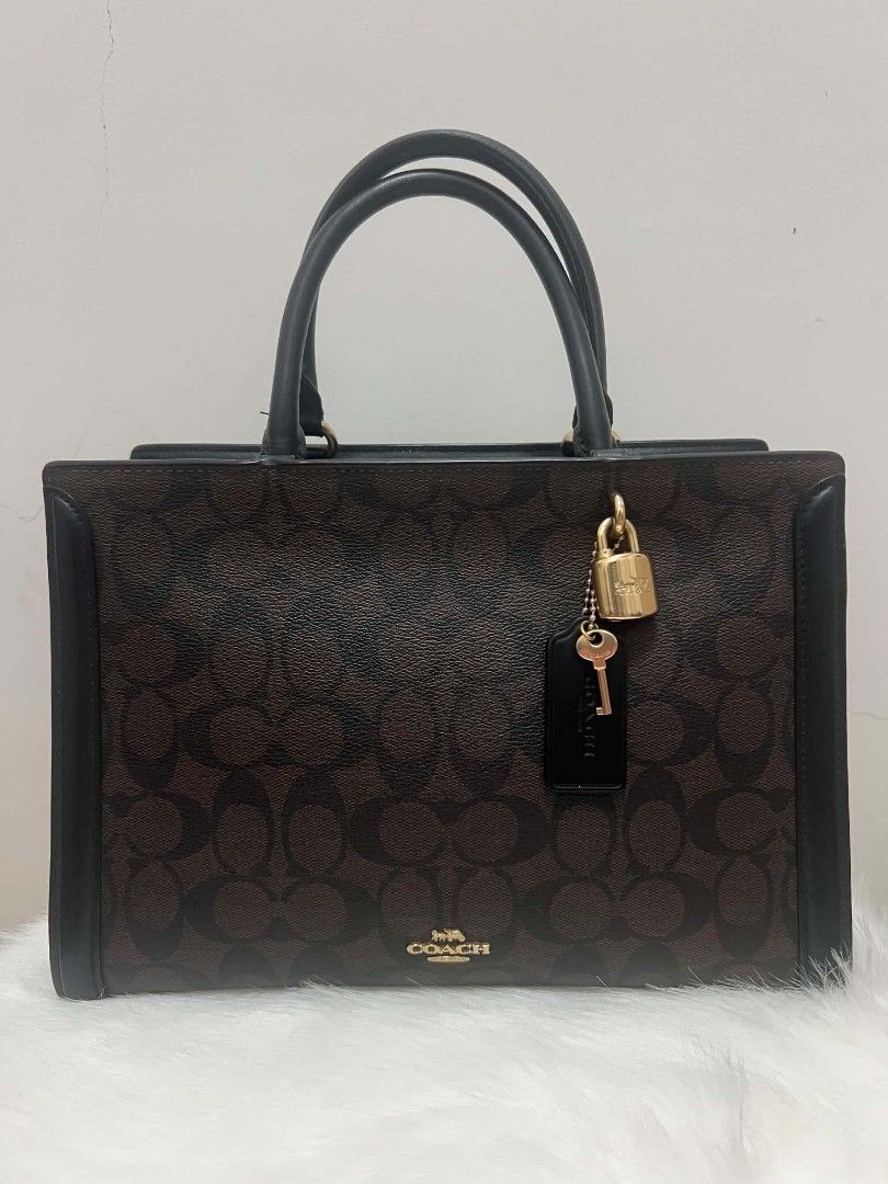 Coach Signature Bag with Lock and Strap (Category: Cross-body Bags) located in Paoay. Submitted by rvf1230 (Listing ID 1465390491, Image 2). Description: - Authentic Coach tote bag in dark brown signature monogram canvas - Features sleek black leather trim and polished gold-tone hardware - Includes charming hanging padlock and key accents - Comes with a detachable black leather shoulder strap and top handles - Convenient open slip pocket on the b