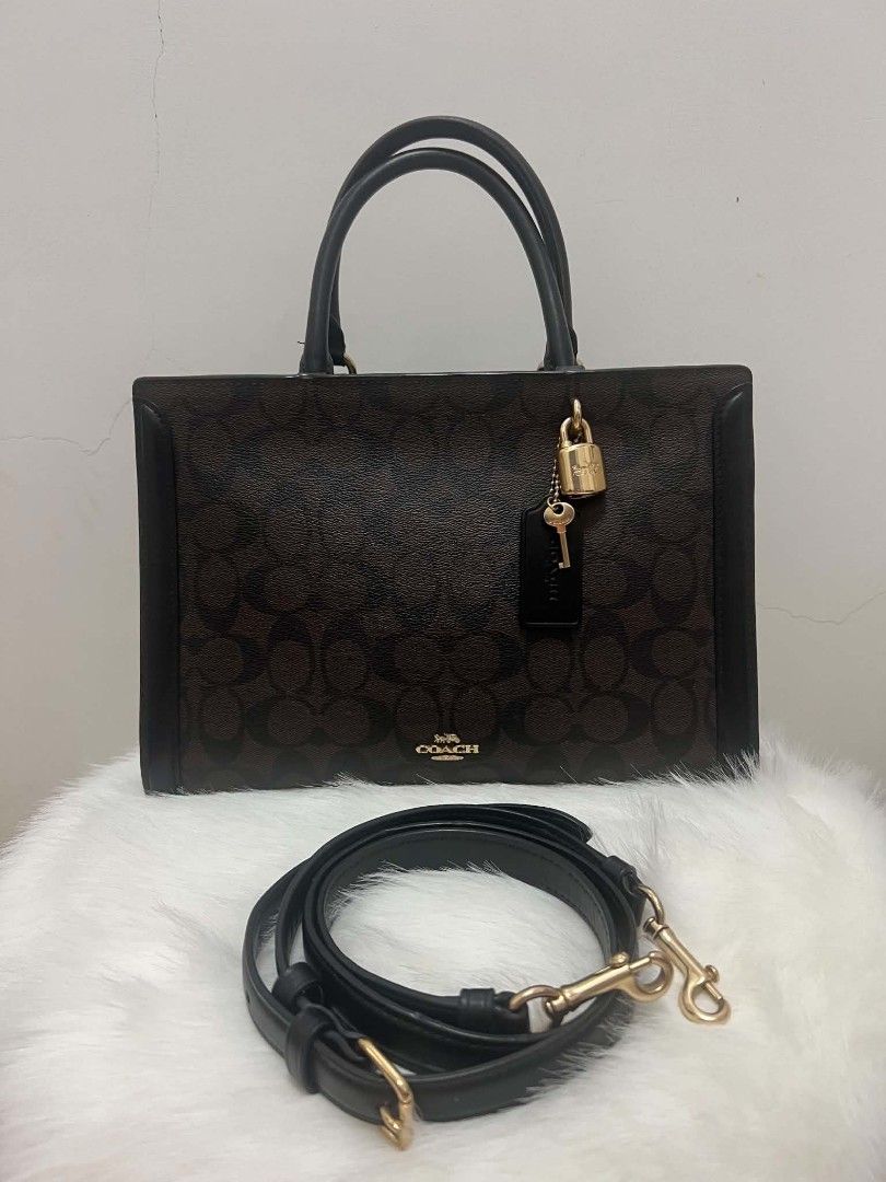Coach Signature Bag with Lock and Strap (Category: Cross-body Bags) located in Paoay. Submitted by rvf1230 (Listing ID 1465390491, Image 1). Description: - Authentic Coach tote bag in dark brown signature monogram canvas - Features sleek black leather trim and polished gold-tone hardware - Includes charming hanging padlock and key accents - Comes with a detachable black leather shoulder strap and top handles - Convenient open slip pocket on the b