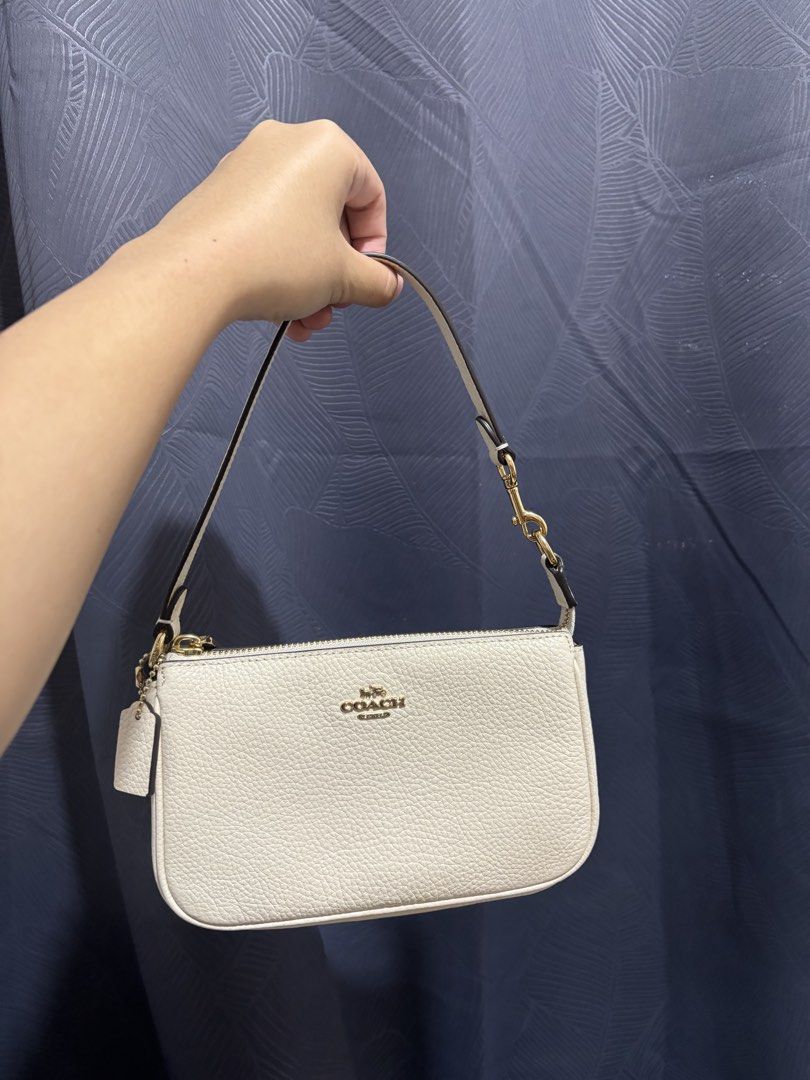 Coach White Nolita 19 (Category: Luxury Bags & Wallets) located in Bulacan. Submitted by janeeeeelleeeee (Listing ID 1465053630, Image 1). Description: - Brand: Coach - Color: Chalk White with gold-tone hardware - Material: Premium textured leather - Condition: Brand new with original store tags attached - Closure: Secure zip-top closure - Versatility: Includes a detachable strap to wear as a shoulder bag or use as a wristlet - Inclusions: Comes 