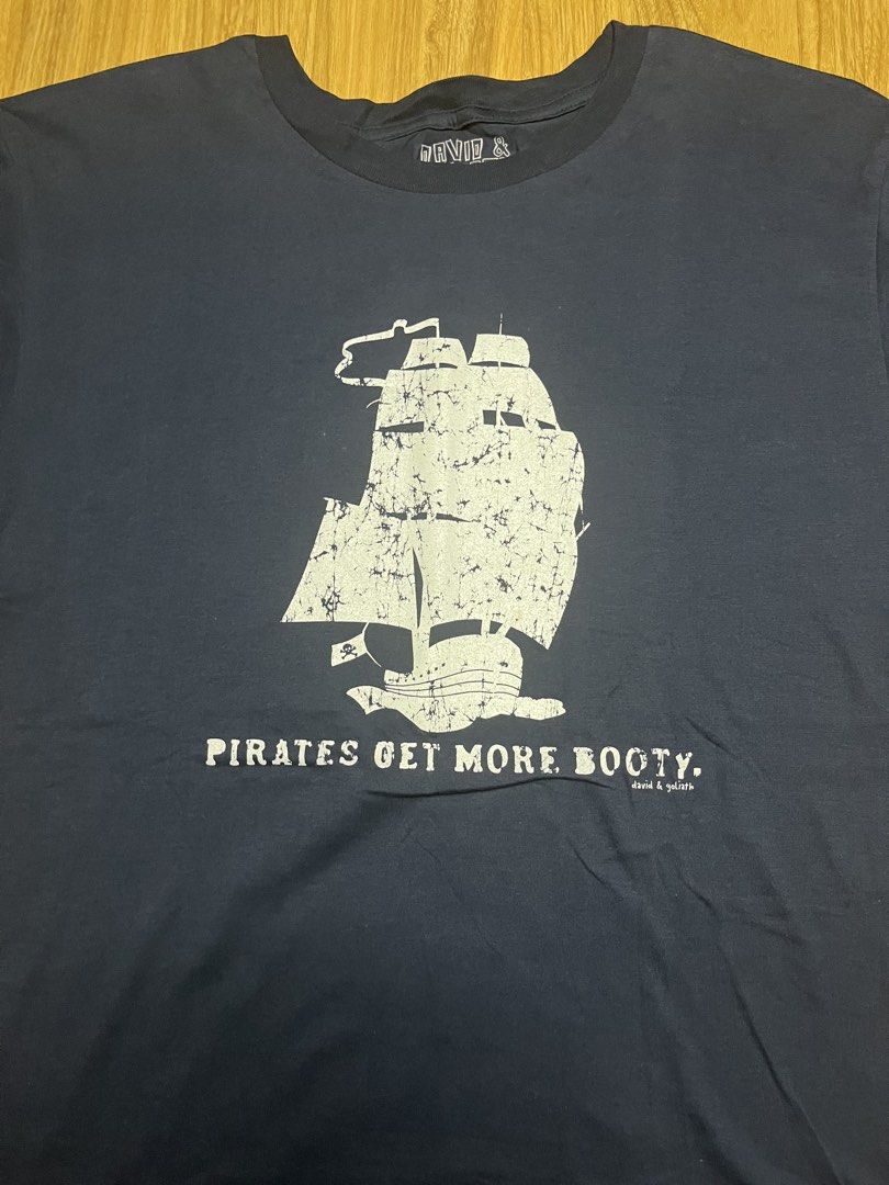 David & Goliath Pirates Get More Booty XL•22x29 (Category: Shirts) located in Cebu City. Submitted by guttathreads (Listing ID 1465429797, Image 2). Description: - Brand: David & Goliath - Color: Navy Blue - Size: XL (inner collar print) - Condition: Brand new with original hang tag attached - Design: Ship graphic with 'Pirates Get More Booty' text on chest - Style: Crew neck, short sleeves - Ideal for casual everyday wear.