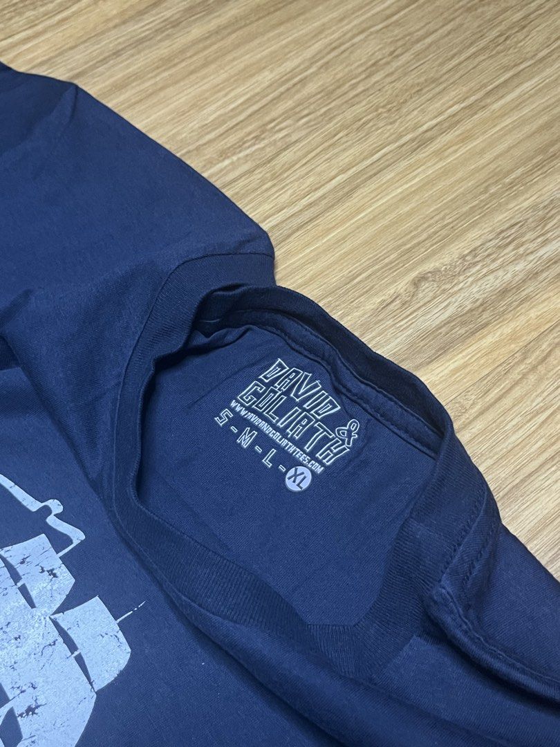 David & Goliath Pirates Get More Booty XL•22x29 (Category: Shirts) located in Cebu City. Submitted by guttathreads (Listing ID 1465429797, Image 3). Description: - Brand: David & Goliath - Color: Navy Blue - Size: XL (inner collar print) - Condition: Brand new with original hang tag attached - Design: Ship graphic with 'Pirates Get More Booty' text on chest - Style: Crew neck, short sleeves - Ideal for casual everyday wear.