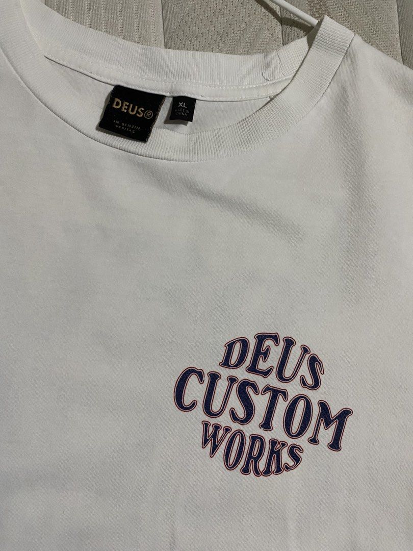 Deus Ex Machina Works Tee (Category: Tshirts & Polo Shirts ) located in Cebu City. Submitted by patspickph (Listing ID 1465424281, Image 3). Description: This is a white Deus Ex Machina Works Tee with a retro graphic on the back and also a print Logo on the Front . Size XL on tag Fits L aswell dimensions W22.5 L30.5 Excellent Condition.