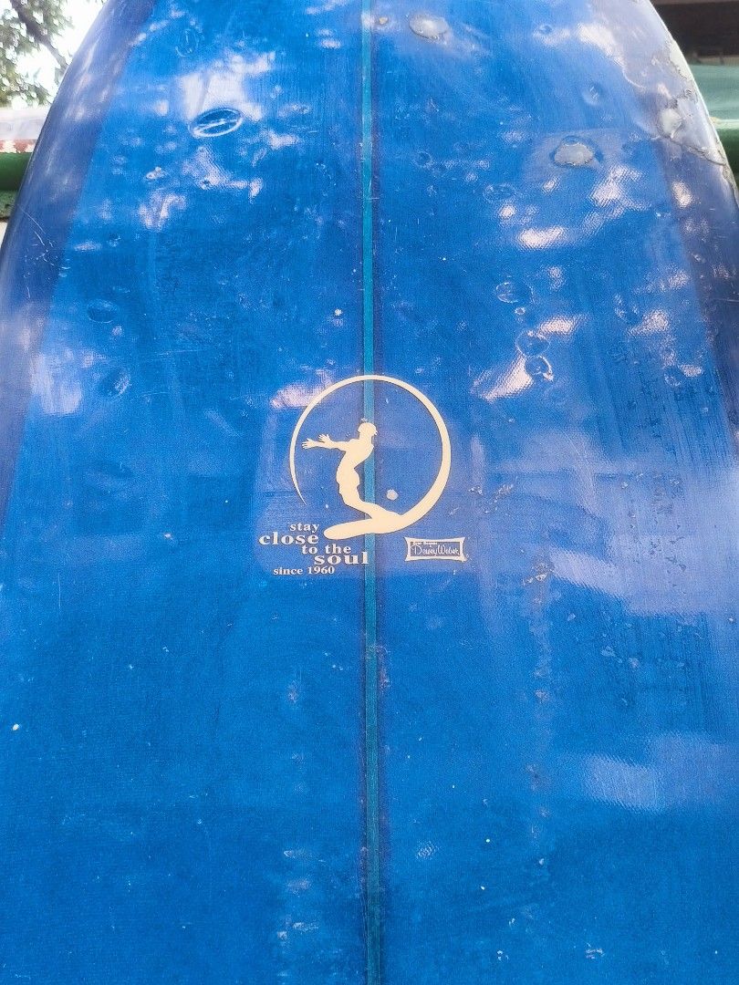 Dewey Weber Longboard Surfboard Blue (Category: Water Sports) located in Manila. Submitted by tonio124 (Listing ID 1465453001, Image 2). Description: - Brand/Model: Dewey Weber classic longboard in deep blue - Design: Features the iconic 'stay close to the soul' logo near the center stringer - Condition: Shows minor dings, pressure bumps, and wax buildup from regular use - Performance: Perfect for smooth wave cruising Board Bag Included - Status: