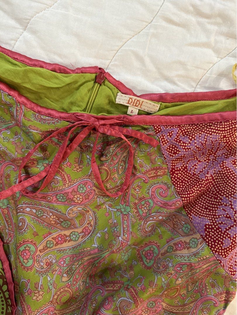 DIDI Multi-pattern Patchwork Wrap Skirt Size L (Category: Skirts) located in Naga. Submitted by maartsy.co (Listing ID 1465428660, Image 2). Description: - Brand: DIDI - Size: L (Tag attached inside waistband) - Design: Boho patchwork with green paisley, red floral dot print, and striped panels - Details: Pink satin trim along the upper edge, matching tie strings, and side zipper closure - Hemline: Asymmetrical with layered fabric details - Condi